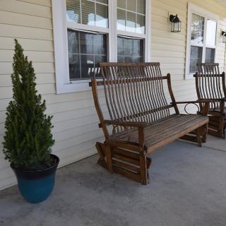 Wooden glider benches on a porch with potted plants.