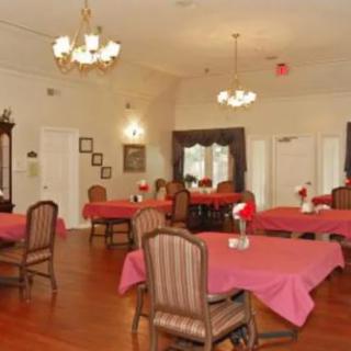 An elegant dining room with tables covered in red tablecloths and classic wooden chairs, lit by chandeliers.