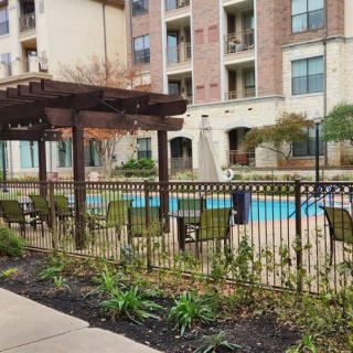 A view of an apartment complex with a fenced outdoor pool area and a pergola.