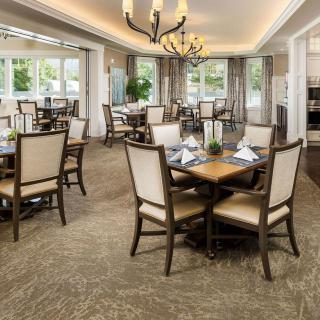 Elegant dining room with neatly arranged tables and chairs, featuring a chandelier and large windows.