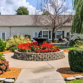 A beautifully landscaped garden with vibrant flowers and a central fountain in front of a house.
