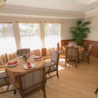 A bright dining room with neatly set tables, wooden chairs, and large windows allowing sunlight to flood the space.