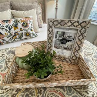 A cozy bedroom setup featuring a decorative tray with a photo frame, a small plant, and a candle on the bed.