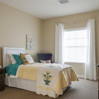 A cozy and well-decorated bedroom with a neatly made bed, accent pillows, and natural light coming through the window.