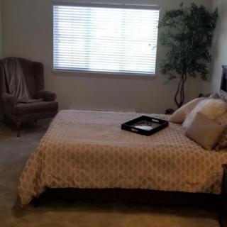 A cozy bedroom with a bed, chair, and plant near the window.
