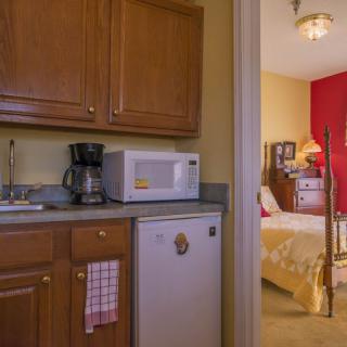 A small kitchenette with a microwave, coffee maker, and mini fridge next to a cozy bedroom.