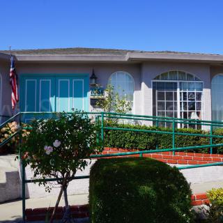 A residential house with a wheelchair ramp and a well-maintained garden, featuring an American flag and large windows.