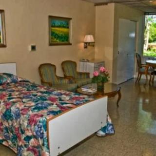 A cozy bedroom with floral bedding, comfortable chairs, and decorative paintings on the wall.