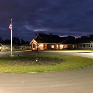 A warmly lit building at night with a flagpole and circular driveway in the foreground.
