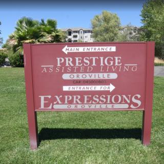 A directional sign for Prestige Assisted Living and Expressions, located on a grassy lawn.