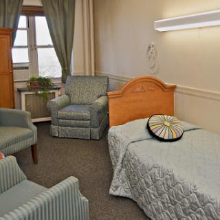 A cozy bedroom setting with a single bed, armchairs, and ambient lighting.