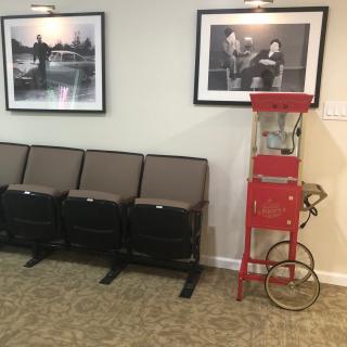 A retro-themed waiting area featuring theater-style seats, a vintage popcorn machine, and framed photographs on the wall.