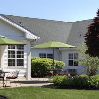 A serene outdoor patio featuring a well-kept garden, complete with green umbrellas and comfortable seating.