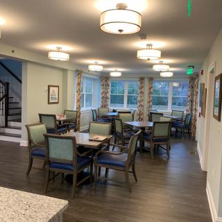 A well-lit dining area featuring multiple tables and chairs, surrounded by large windows.