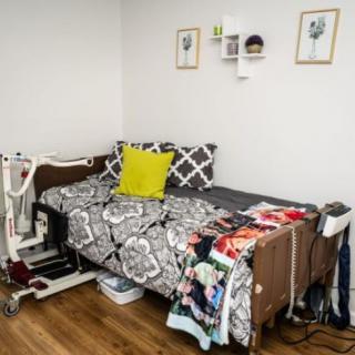 A cozy bedroom with a hospital bed adorned with patterned bedding and pillows, featuring wall art and wooden flooring.
