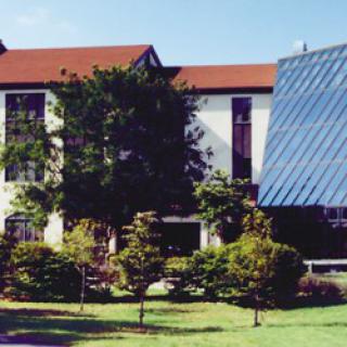 A modern building with a glass facade surrounded by trees and greenery.