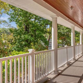 A spacious porch with white columns and railing overlooking lush green trees.