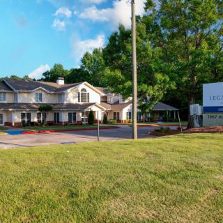 A large residential building with a sign, surrounded by trees and grass under a blue sky.