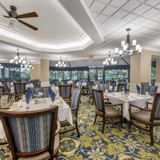 An elegant dining room with neatly arranged tables and chairs, featuring chandeliers and a floral carpet.