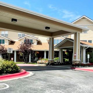 The image shows a building entrance with a covered driveway and landscaped surroundings.