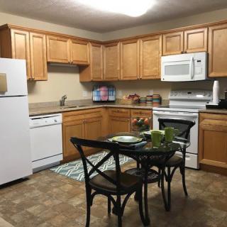 A cozy kitchen with wooden cabinets, featuring modern appliances and a small dining table.