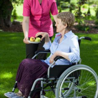 A caregiver offers fruit to a person in a wheelchair outdoors.