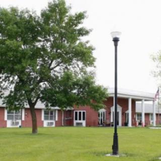 A brick building with large windows, a tree, and a lamp post on a grassy area.