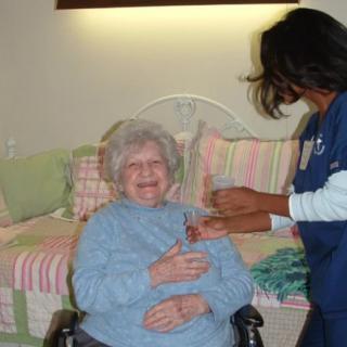 A nurse assists a smiling elderly woman seated in a wheelchair.