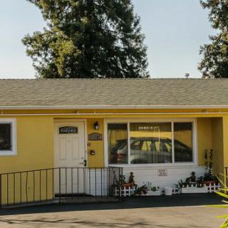 A yellow single-story house with a front porch and driveway, set against a backdrop of trees.