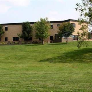A view of a building with a large grassy lawn and several trees under a clear sky.