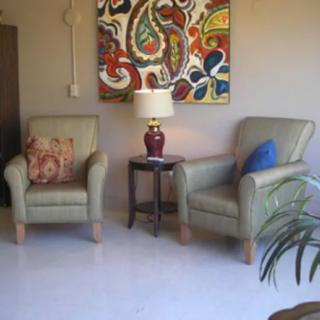 A cozy living room with two armchairs, a colorful abstract painting, and a lamp on a side table.