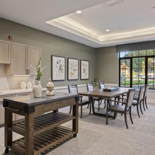 A modern dining room with a large table, chairs, and a kitchen island, accented by wall art and ample natural light.
