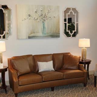 A cozy living room with a brown leather sofa, decorative art pieces, mirrors, and table lamps.