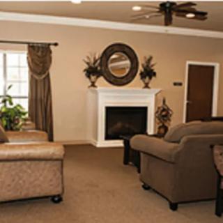 A cozy living room with comfortable sofas and a fireplace, accented by decorative plants and a mirror above the mantel.