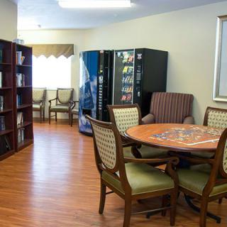 A cozy reading and relaxation area featuring a table with chairs, bookshelves, and vending machines.