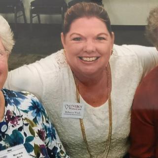 A group of people smiling at an indoor gathering, wearing name tags.