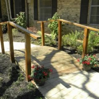 A wooden ramp with handrails leading to a building entrance, surrounded by a garden.