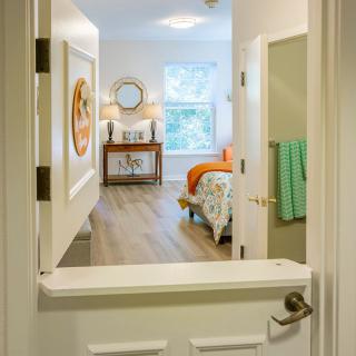 A view through an open doorway into a cozy bedroom featuring bright decor and natural lighting.
