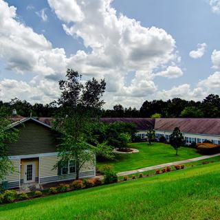 A picturesque countryside scene with a house surrounded by lush greenery and a cloudy sky.