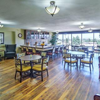 A spacious dining area with wooden floors, tables, and chairs, featuring a bar and large windows.