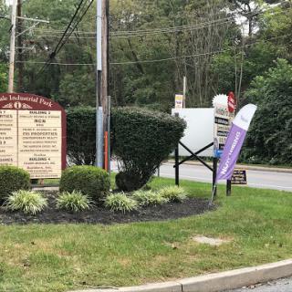 A view of a roadside business sign surrounded by greenery and landscaping.