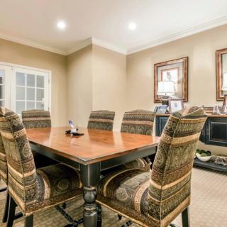 A well-appointed dining room with a large wooden table surrounded by upholstered chairs, featuring warm lighting and decorative artwork.