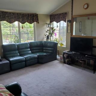 A cozy living room with a black leather sectional sofa, large windows, and a television on a stand.