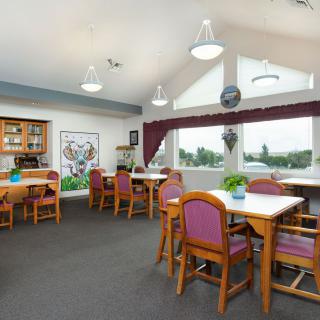 A spacious dining room with multiple tables and chairs, featuring large windows and decorative elements.