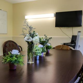 A well-decorated conference room featuring a wooden table adorned with floral arrangements, a television for presentations, and a warm ambiance.