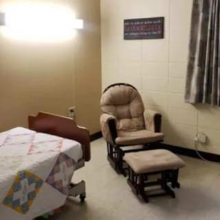 A hospital room with a bed, cushioned chair, and footstool.
