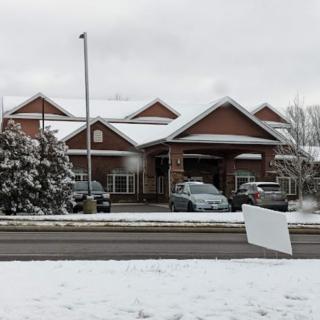 A snow-covered landscape with a building and parked cars on an overcast day.