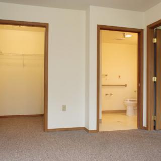 An empty room with a carpeted floor, featuring doorways leading to a closet and a bathroom.