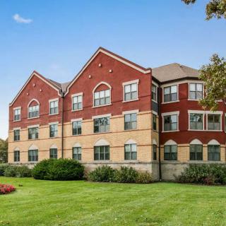 A brick residential building with arched windows and a well-maintained lawn in front.