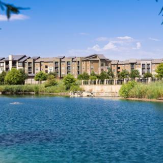 A scenic view of residential buildings by a tranquil lake surrounded by greenery.
